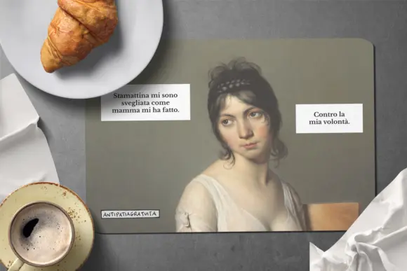 Tovaglietta americana Antipatiagratuita su una superficie grigia, con un croissant su un piatto, una tazza di caff&egrave; e un tovagliolo bianco. Sopra, il ritratto di una giovane donna d&rsquo;inizio Ottocento dallo sguardo scocciato con i fumetti &ldquo;Stamattina mi sono svegliata come mamma mi ha fatto.&rdquo; e &ldquo;Contro la mia volont&agrave;.&rdquo;