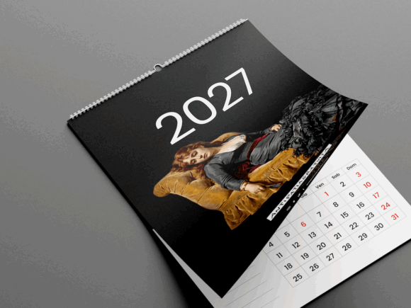 Calendario da parete 2027 Antipatiagratuita appoggiato su una superficie grigia, con la copertina nera sollevata che lascia intravedere la griglia di gennaio. In copertina la scritta “2027” e il dipinto di una donna sdraiata su una chaise longue dorata.