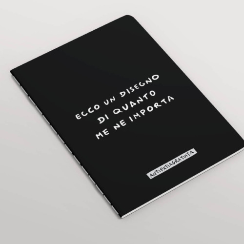 Quaderno nero con angoli arrotondati e cucitura a vista, inclinato in prospettiva su sfondo grigio chiaro. In copertina la frase scritta a mano in bianco “Ecco un disegno di quanto me ne importa” e, in basso, l’etichetta “Antipatiagratuita”.