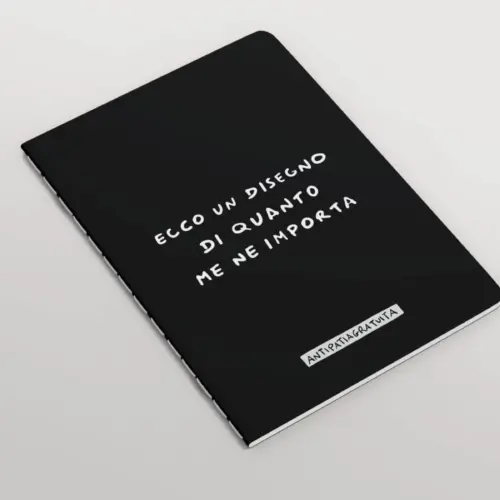 Quaderno nero con angoli arrotondati e cucitura a vista, inclinato in prospettiva su sfondo grigio chiaro. In copertina la frase scritta a mano in bianco “Ecco un disegno di quanto me ne importa” e, in basso, l’etichetta “Antipatiagratuita”.